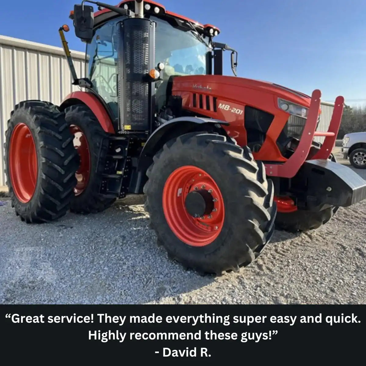 Red tractor with large black and red tires on a gravel surface, with a blue sky in the background.